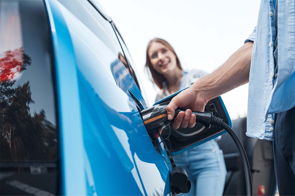 photo of man inserting plug into electric vehicle while woman looks on