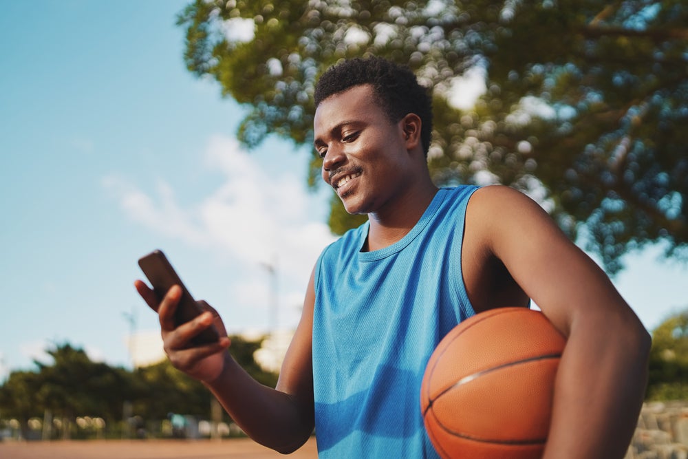 young man looking at mobile phone with basketball under his arm